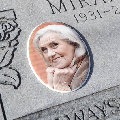 Oval headstone picture of woman placed on a flat grave marker. Oval porcelain memorial plaque of woman with white hair resting her chin on her hands.